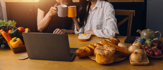 Happy two young women looking laptop computer during cooking together in kitchen room at home. Two young diverse lesbian women spending time together. LGBT and gender identity concept..
