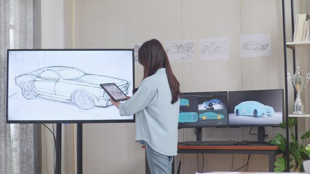 Side View Of Asian Female Comparing Her Car Design On A Tablet To The Photo On Tv While Working In The Studio With Computers Display 3D Electric Car Model 
