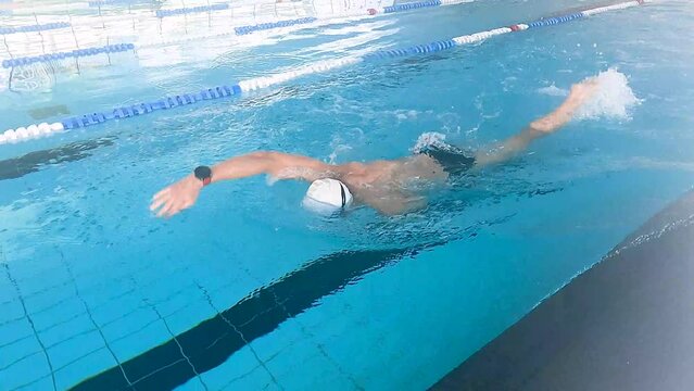 A swimmer with a disabled arm is swimming in a heated pool to train for a championship. Concept of disabled people, swimmers with an amputated arm.