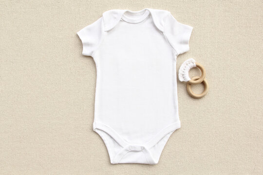 Baby onesie flatlay on a linen fabric with toy. Baby bodysuit mockup. Copy space for your design here.