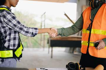 Construction team shake hands greeting start new project plan behind yellow helmet on desk in office center to consults about their building project..