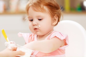 Fototapeta premium A baby eating yogurt with some on her face.