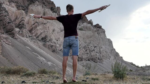 A young thin adult guy has fun and enjoys the strong wind in the mountains, spreading his arms like the wings of a bird in flight. Meditation on the Sadhu Board. Nailing