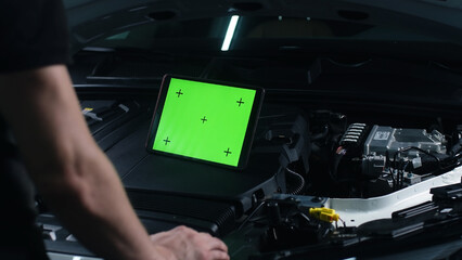 Unrecognizable male car service worker checking car and doing maintenance using a digital tablet computer with green screen chromakey, while standing near the opened bonnet