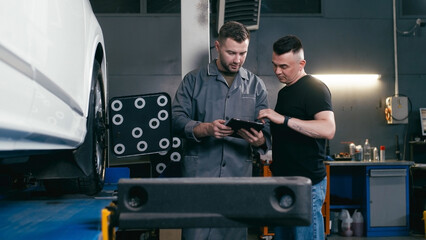 mechanic and service manager in a repair shop near a car diagnosing and checking a car together in a car service, using a tablet and discussing repairs