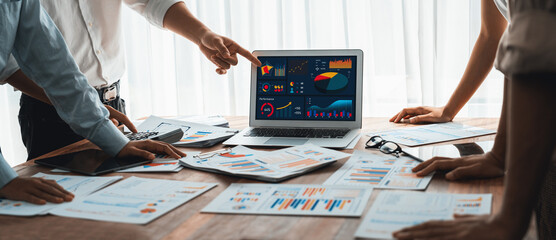Panorama shot analyst team utilizing BI Fintech to analyze financial report with laptop. Businesspeople analyzing BI power dashboard displayed on laptop screen for business insight. Scrutinize