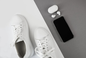 white sneakers with headphones and a smartphone on a gray-white background.