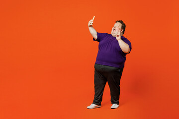 Full size body young chubby overweight man in purple t-shirt casual clothes do selfie shot on mobile cell phone post photo on social network isolated on plain red orange background Lifestyle concept