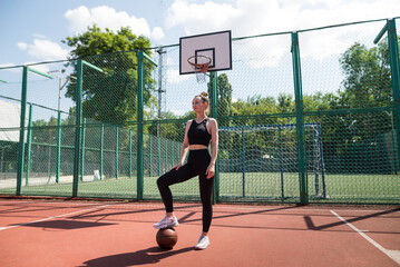 Obraz premium Young sports girl with a basketball on the basketball court outdoors,