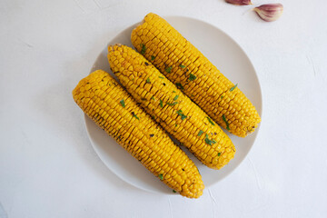 Corn on a white plate, cooked, baked with herbs and spices on a light background, top view. Proper nutrition.