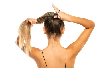 Young beautiful woman tying her hair in a ponytail on a white studio background