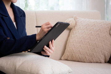 Closeup hands young asian businesswoman sitting on sofa using tablet computer for planning success business in living room at home office, business woman relax while writing on digital tablet.