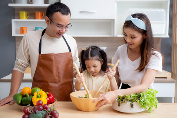 Happiness asian family with father, mother and daughter preparing cooking salad vegetable food together in kitchen at home, happy dad, mom and kid cooking breakfast with salad, lifestyles concept.