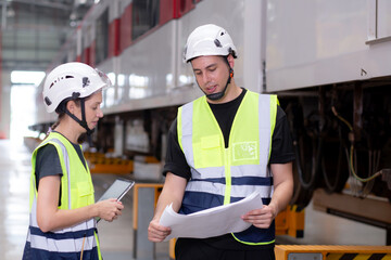 Young caucasian engineer man and woman or worker look blueprint and checking electric train for planning maintenance in station, transport and infrastructure, inspector or technician check transport.