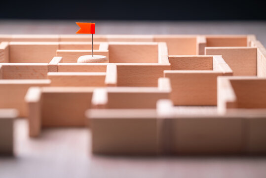 Goal hidden in the labyrinth, maze game with flag push pin built by wooden pieces, complex way to reach the target, success and challenge
