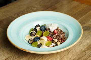 A bowl of cereal with fruits on a wooden table