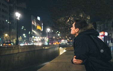 Young caucasian man leaning on a low stone wall on the street at night