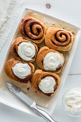 A platter of freshly baked cinnamon buns with frosting on four.