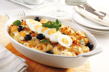 Baked cod with onion, black olives, boiled eggs and oregano. In an oval iron baking dish....