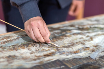 Restorer artist restore paint on picture. Close-up of hand holds brush. Selective focus. Cultural...