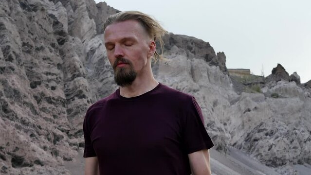 Portrait of a young attractive man meditating in the mountains with a strong wind holding shiny black obsidian stones in both hands. Meditation with stones. The power of stones and volcanic glass