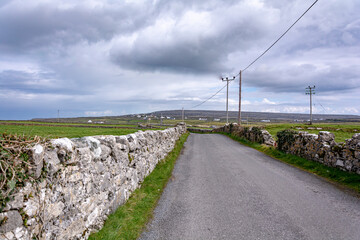 Fototapeta na wymiar Scenic road with stone walls alongside on a bright sunny day with a clouds and blue sky on Inishmore island, Galway