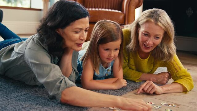 Same sex family with two mature mums and daughter lying on floor doing jigsaw puzzle together - shot in slow motion