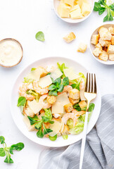 Gourmet Caesar salad with shrimp, iceberg and lettuce, croutons, parmesan cheese and caesar dressing. White table background, top view