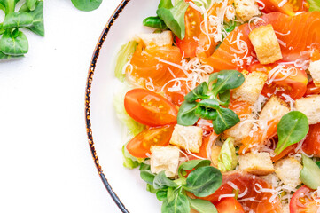 Delicious caesar salad with salmon, iceberg and lettuce, croutons, parmesan cheese and caesar dressing. White table background, top view