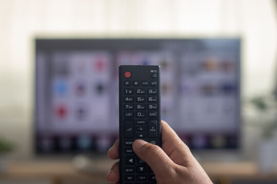 The man is watching TV and using a remote control to search for a program on the internet.