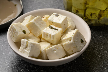 Bowl with white cheese cubes in oil and herbs close up as an ingredient 
