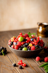 Various fresh berries in a bowl. Mix of different fresh berries on wooden background. Strawberries, raspberries, gooseberries and cherries are presented.