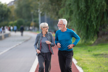 Cheerful active senior couple jogging together outdoors along the river. Healthy activities for elderly people.