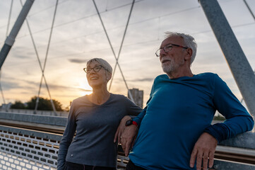 Cheerful active senior couple jogging together outdoors on the bridge. Healthy activities for elderly people.
