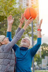 Cheerful active senior couple playing basketball on the urban basketball street court. Happy living after 60.