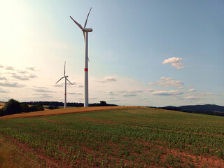 Windenergie: Windräder in der Natur zwischen Wiesen und Feldern bei leicht bewölktem Himmel bei...