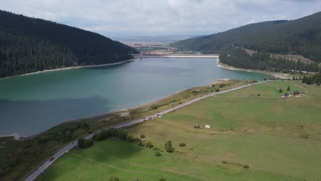 Aerial footage of Lake Barajul Frumoasa and evergreen trees in front of a local community