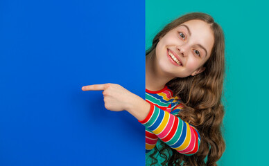 happy teen child behind blank blue paper with copy space for advertisement. point finger