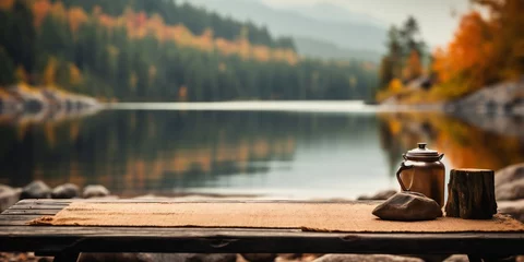 Fototapete Khaki Wooden table with teapot in front of blurred background of autumn forest and lake. Lake, mountains and forest.