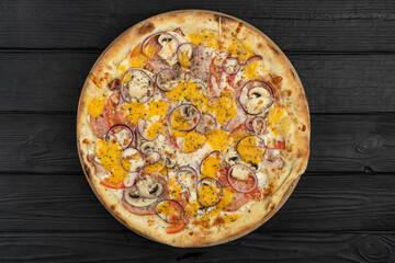 Top view of hot pizza on black wooden background, with onions, bacon and cherry tomatoes, thin pastry crust, closeup.