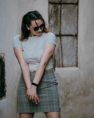 Vertical shot of a brunette woman wearing a skirt and sunglasses posing on the street