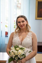 Beautiful bride holding a bouquet standing next to the wooden table in her wedding dress