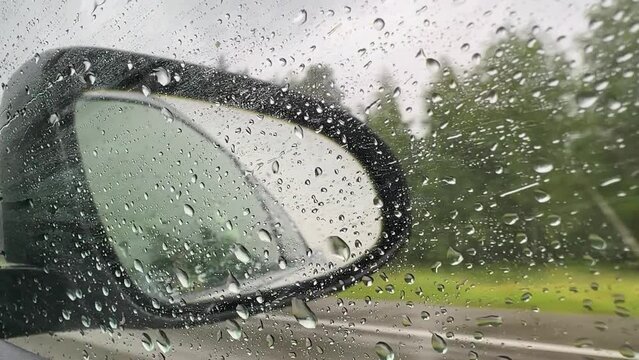 Rain drops fall on the side window and mirror of a car. Reflection of side-view mirror of car driving on rainy day