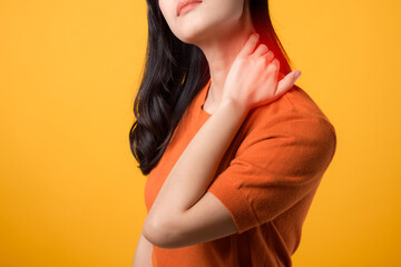 Supportive young Asian woman in her 30s, wearing an orange shirt, holds her pain neck on yellow...
