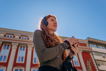 Low angle view shot of lovely ginger girl with headphones on, holding a phone and looking away