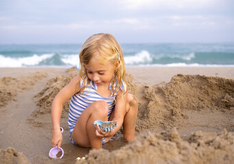 Cute three years old girl playing with sand at beach, seaside in Spain.Happy kid on vacation in summer.Copy space.