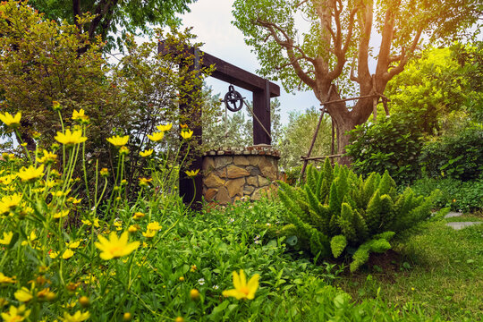 Beautiful artesian well made by stones and wheel pulley with metal bucket and rope in peaceful garden atmosphere. Retro stone water well in rural area. Beautiful garden decoration with antique items.