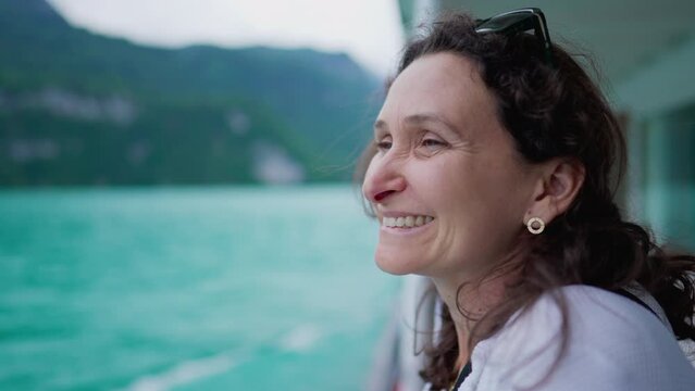 Happy woman traveling by boat observing lake and mountain view, enjoying vacations, close-up face of joyful female person in 40s feeling serene and peaceful