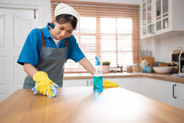 Asia woman in workwear maid cleaning home holding bottle spray and wiping with microfiber cloth in kitchen room at home	