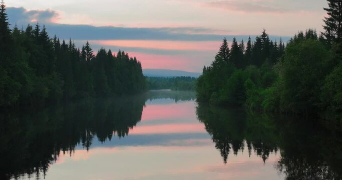 Aerial video of the lake reflecting a forest during pink sunset